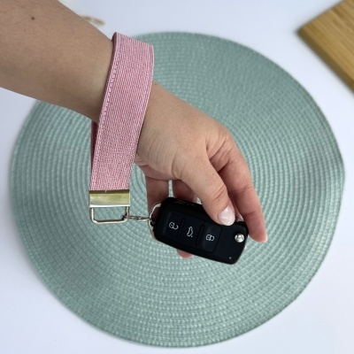 Chave de carro preta com chaveiro rosa claro numa mão sobre tapete verde claro