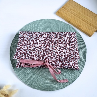 Estojo de tecido floral branco com flores vermelhas e laço rosa sobre prato verde claro