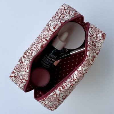 Necessaire floral vinho e branco com frasco Uriage Hyseac, recipiente branco, pincel prateado e recipiente vinho no interior.