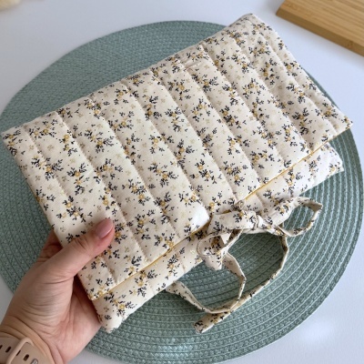 Manta acolchoada creme com flores pequenas e laços, segurada por mão