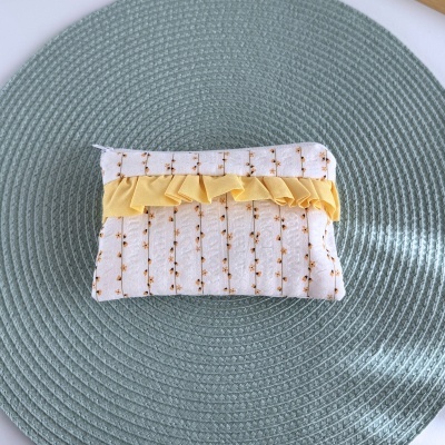 Necessaire retangular em tecido branco com flores amarelas e folho amarelo sobre tapete verde