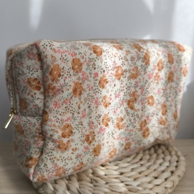 Bolsa de tecido floral creme com fecho dourado sobre base trançada de palha