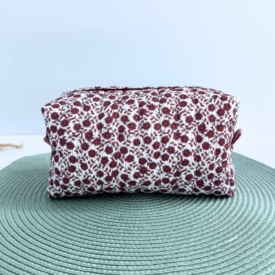 Mala de tecido floral vermelha e branca sobre tapete verde