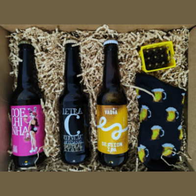 Caixa com três garrafas de cerveja, cesto amarelo com tampas e meias pretas com padrão de canecas de cerveja