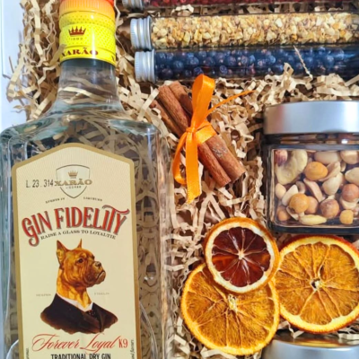Garrafa de gin com rótulo de cão, tubos de ensaio com frutos secos, paus de canela com fita laranja e fatias secas de laranja num conjunto de presente.