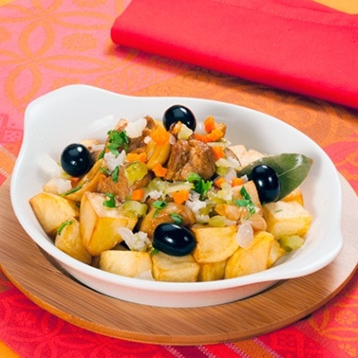 Prato branco com batatas, carne e azeitonas sobre toalha colorida