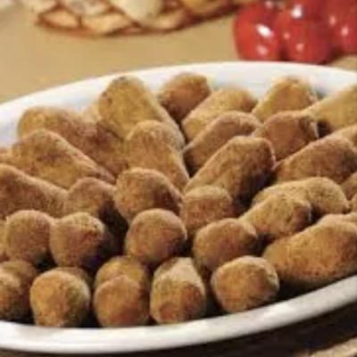 Travessa com palitos e bolinhas douradas, tomates e pão ao fundo