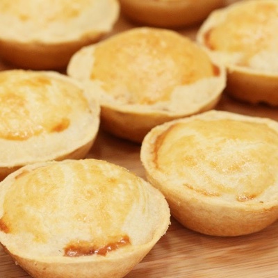 Doze pequenas tartes douradas sobre superfície de madeira