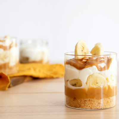 Copos transparentes com sobremesa em camadas com banana, creme, doce castanho e base triturada