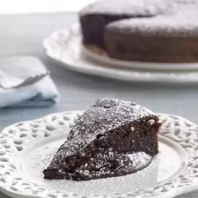 Fatia de bolo de chocolate polvilhado com açúcar em pó num prato branco.