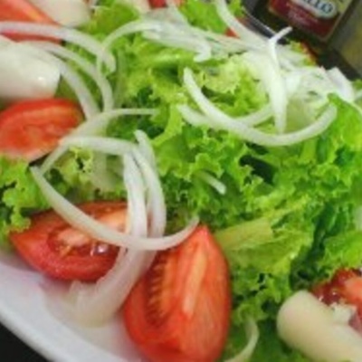 Prato branco com salada de folhas verdes, tomate, cebola e alho