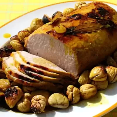 Travessa oval com carne assada fatiada rodeada de castanhas e ameixas secas