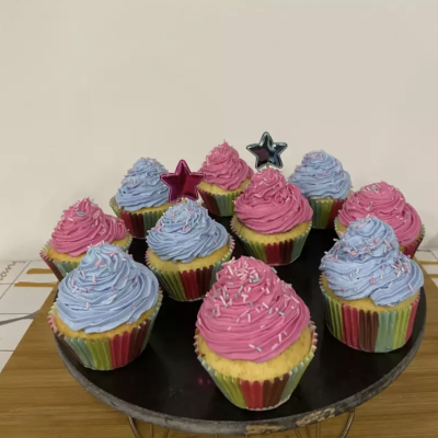 Doze cupcakes com creme rosa e azul em suporte preto sobre madeira.
