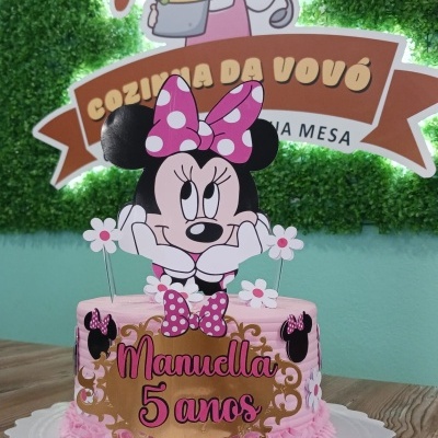 Bolo rosa com decoração Minnie Mouse e texto Manueilla 5 anos em fundo de madeira