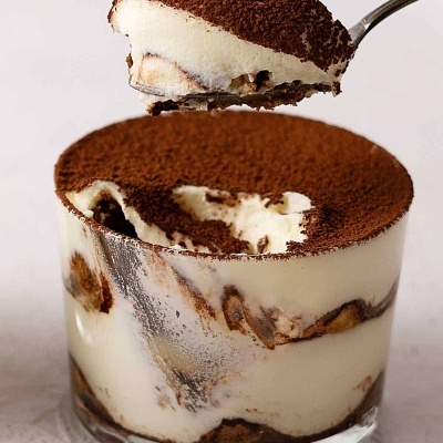 Copinho de tiramisu com camadas visíveis e colher a levantar uma porção.