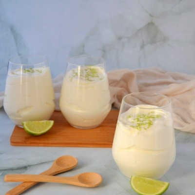 Copos com creme branco decorados com raspas verdes e fatias de lima ao lado em superfície de mármore cinza