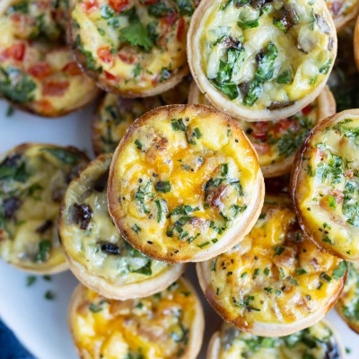 Mini quiches com queijo, ovos, ervas e legumes num prato branco