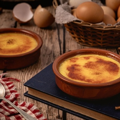 Creme queimado em travessas de barro com ovos e pau de canela numa mesa de madeira rústica
