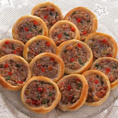 Doze empadas redondas com recheio de carne e pimentos num prato de vidro sobre uma toalha com estrelas