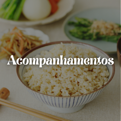 Tigela com arroz cozido e pratos de legumes ao fundo com pauzinhos de madeira em superfície clara