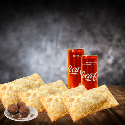 Latas de Coca-Cola, pastéis dourados e brigadeiros num prato branco sobre mesa de madeira.