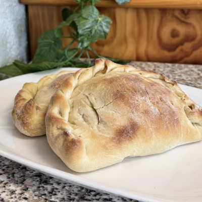 Dois pastéis assados dourados em prato branco sobre superfície de pedra com fundo de madeira e folhas verdes