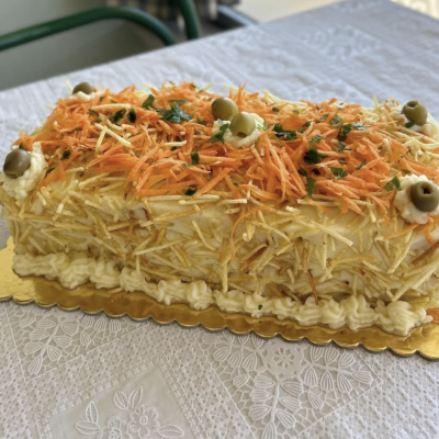 Salada tipo bolo coberta com batata palha, cenoura, azeitonas e salsa em prato dourado, sobre toalha branca