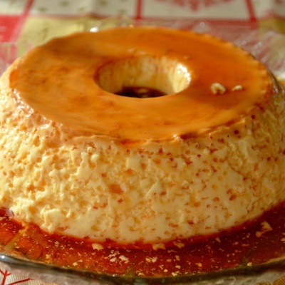 Pudim com caramelo servido num prato de vidro sobre uma toalha vermelha e branca com padrões festivos