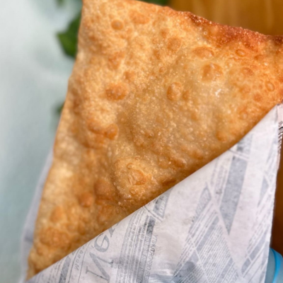 Pastel frito dourado embrulhado em papel estilo jornal, segurado com luva azul