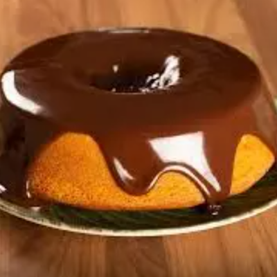 Bolo anel com cobertura de chocolate sobre prato branco e madeira clara