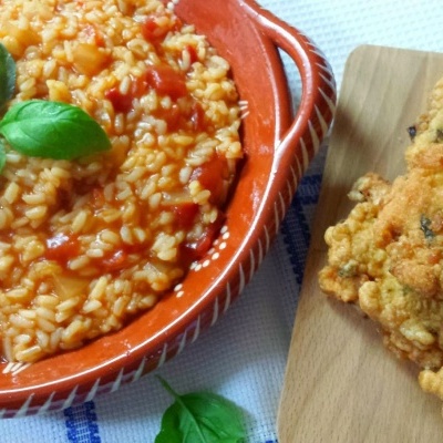 Risoto de arroz vermelho em prato cerâmico castanho com pastéis fritos em tábua de madeira