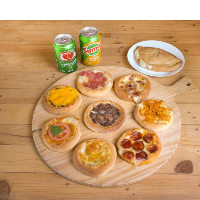 Mini pizzas variadas e pastel em prato com latas de refrigerante Guaraná e Sumol laranja numa mesa de madeira