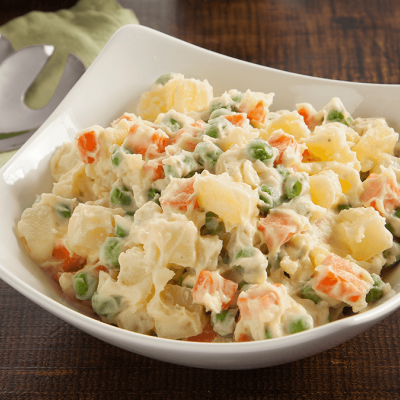 Salada de batata com cenoura e ervilhas numa taça branca com talheres ao lado