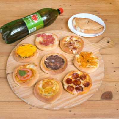 Mini pizzas variadas numa tábua de madeira com pastel e garrafa de refrigerante SUMOL