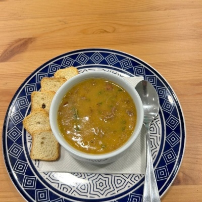 Sopa amarelada em tigela branca com pão torrado sobre prato azul e branco