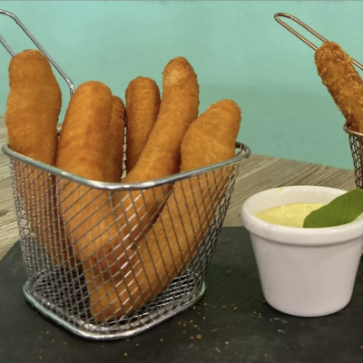 Snacks fritos crocantes em cestos metálicos com molho cremoso num recipiente branco em fundo azul claro.