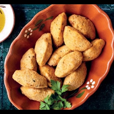 Travessa de barro com pastéis fritos dourados e pratos com azeite e grãos amarelos