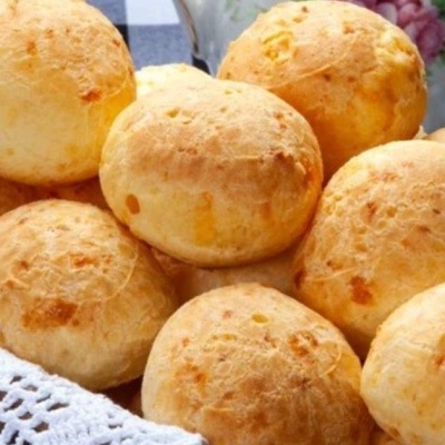 Pães de queijo dourados em cesto com toalha branca rendada