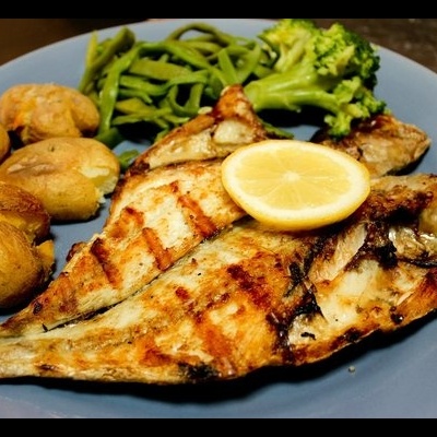 peixe grelhado com limão, batatas, feijão verde e brócolos num prato azul