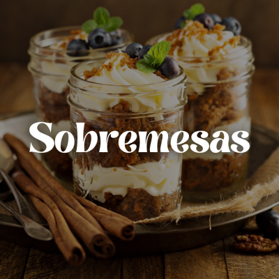 Três frascos de sobremesa com creme, bolo, mirtilos e hortelã numa bandeja de metal sobre mesa de madeira.
