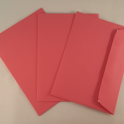 Quatro envelopes cor-de-rosa, um aberto, sobre superfície bege