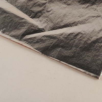 Folha metálica prateada parcialmente amassada sobre superfície branca