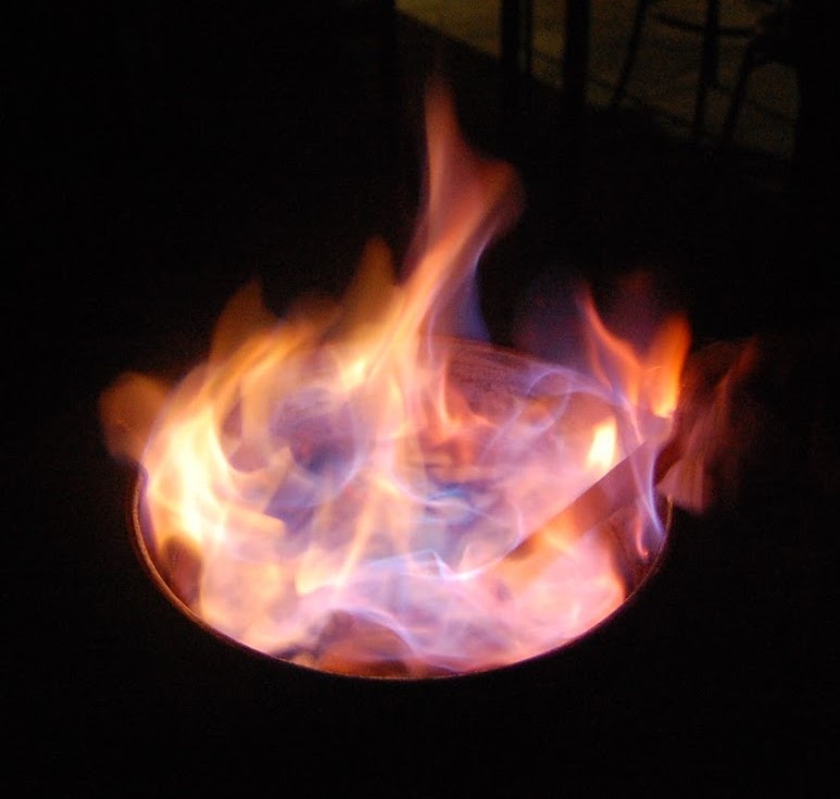 Chama de fogo colorida numa estrutura metálica redonda preta em ambiente escuro