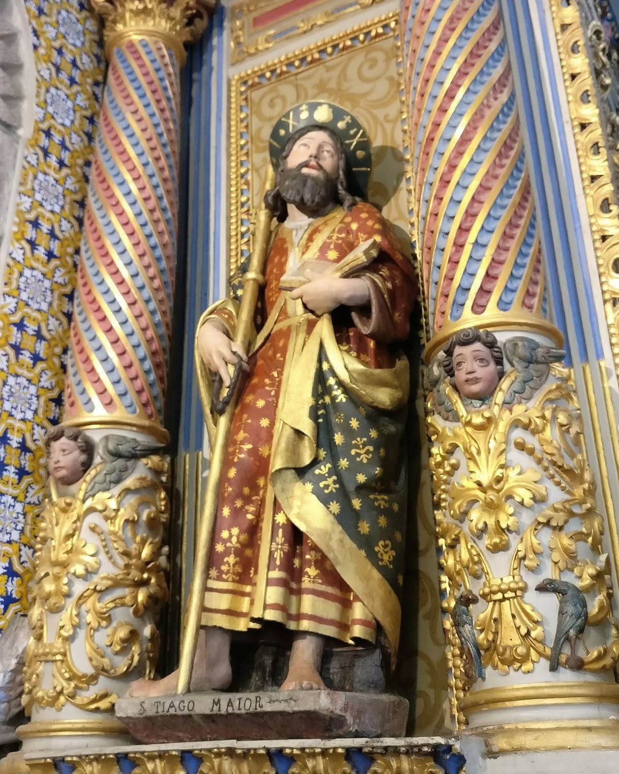Estátua de S. Tiago Maior em túnica vermelha e manto azul com detalhes dourados entre colunas decoradas