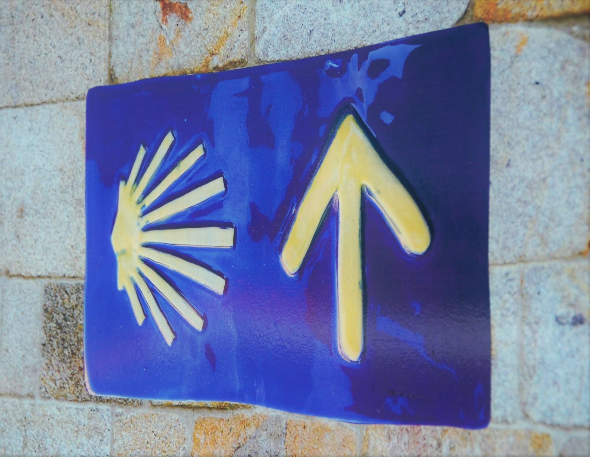 Placa azul com concha amarela e seta amarela numa parede de pedra