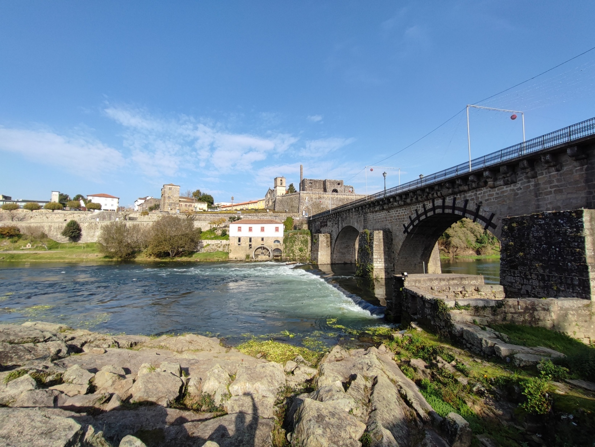 Ponte em pedra sobre rio com céu azul e rochas na margem