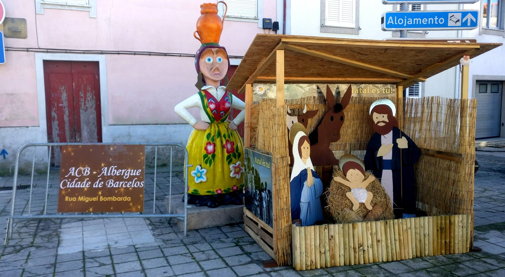 Presépio artesanal de madeira com figuras pintadas e estátua colorida feminina em rua urbana
