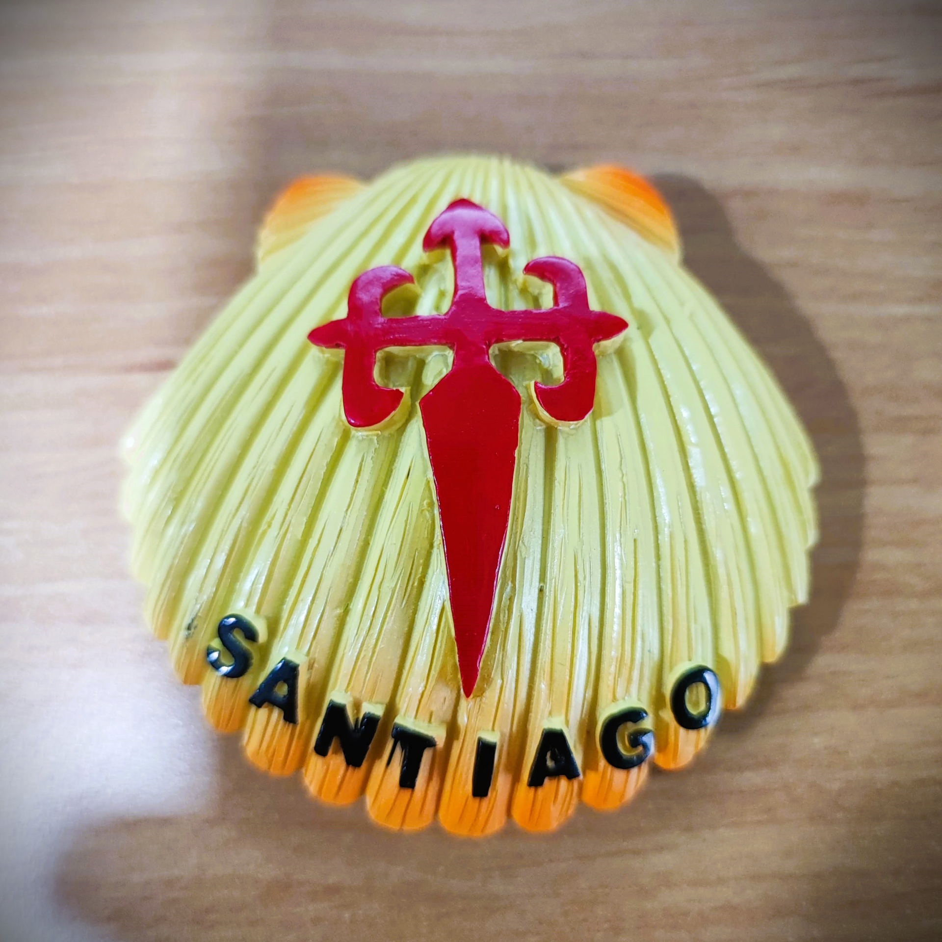 Íman (Vieira Santiago) Concha decorativa amarela com texto SANTIAGO e símbolo vermelho