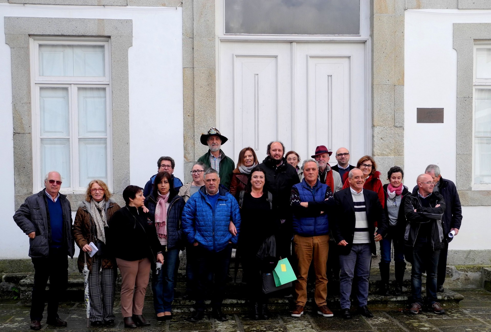 Grupo de pessoas em frente a prédio branco com porta e janelas