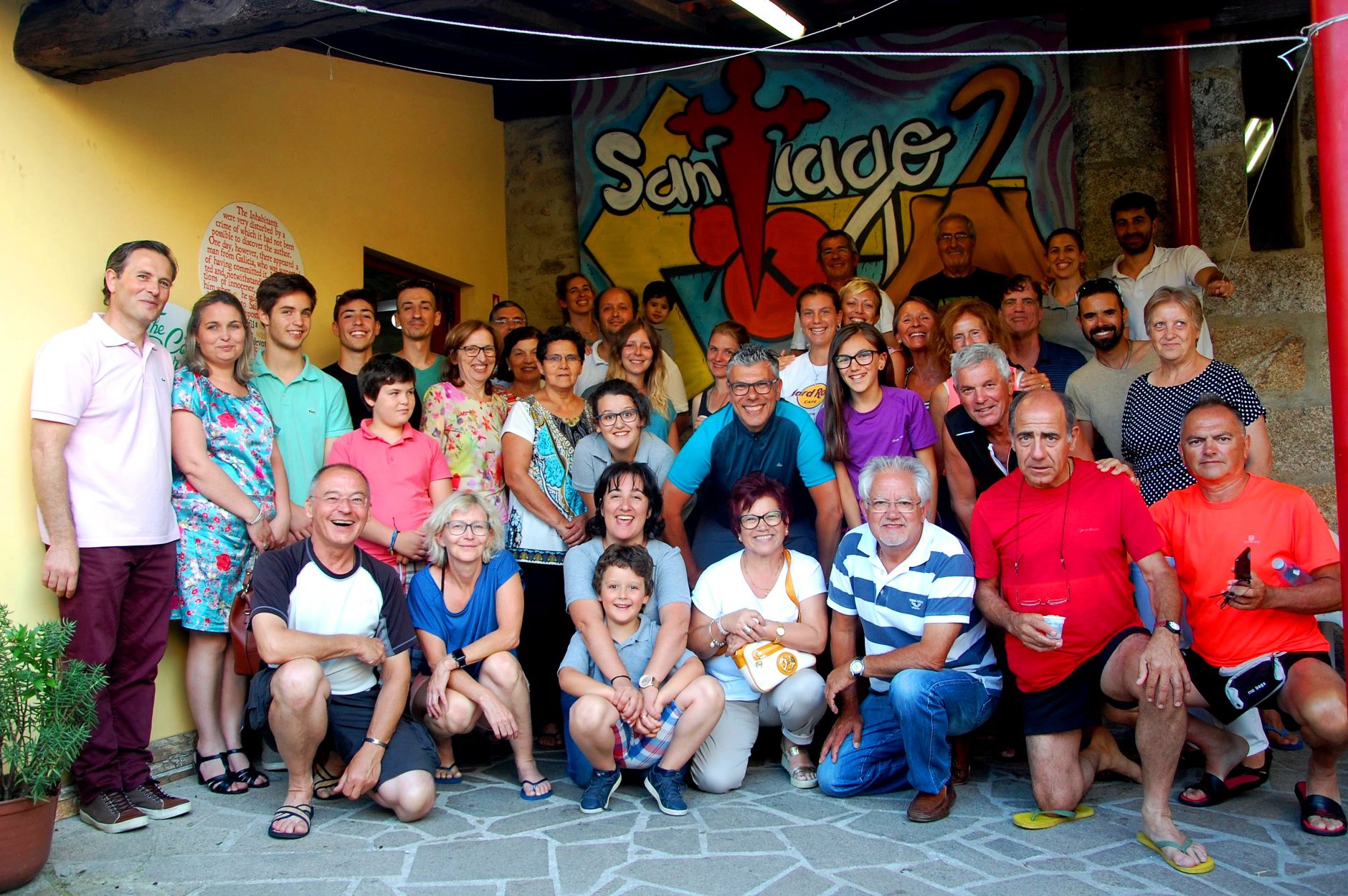 Grupo grande de pessoas posando em pavimento de pedra com mural colorido ao fundo